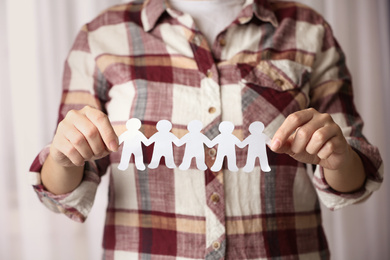 Photo of Woman holding paper people chain indoors, closeup. Unity concept