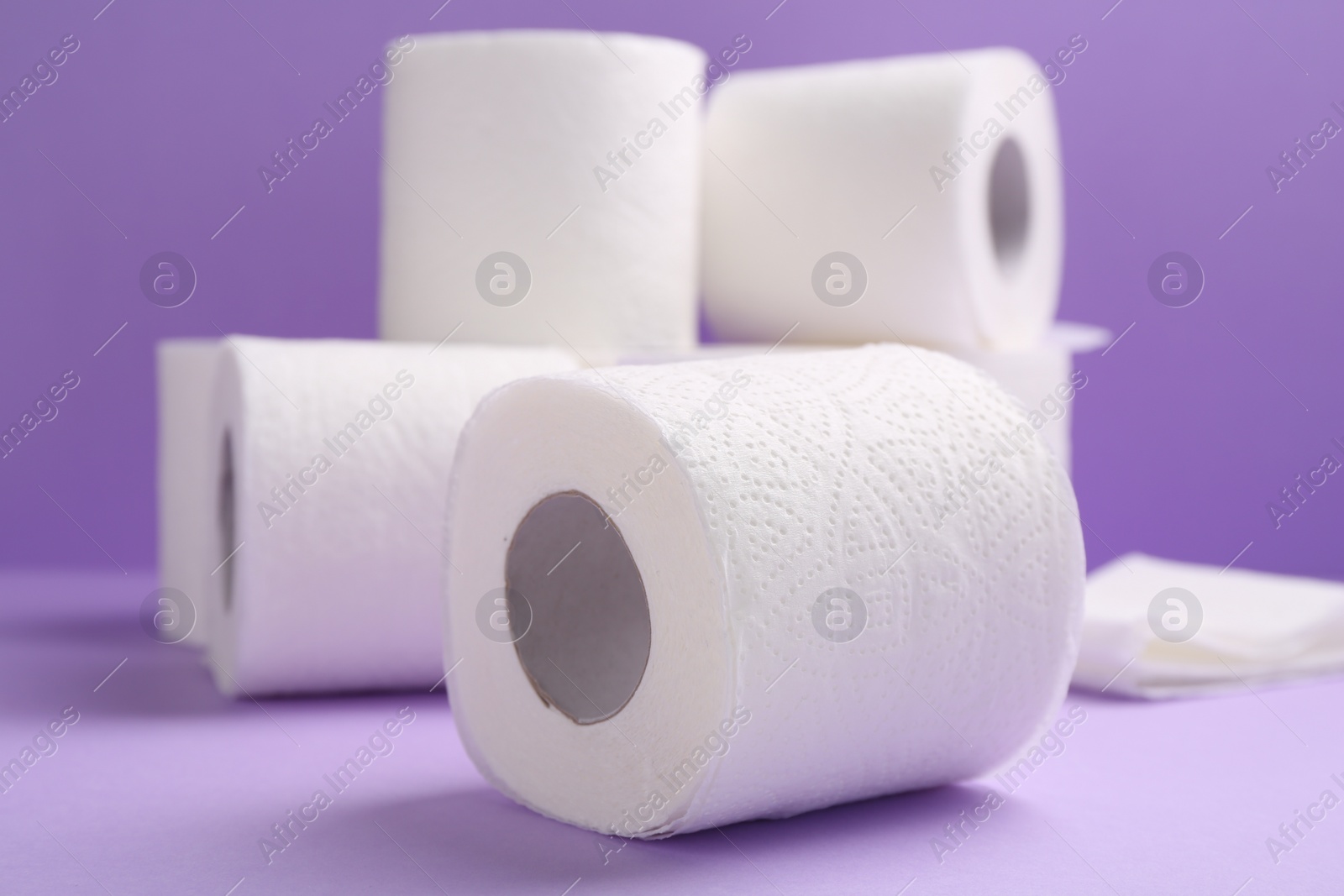 Photo of Soft toilet paper rolls on violet background, closeup