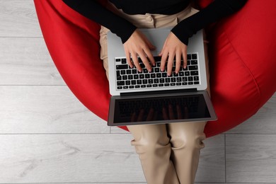 Photo of Woman working with laptop in beanbag chair, top view. Space for text