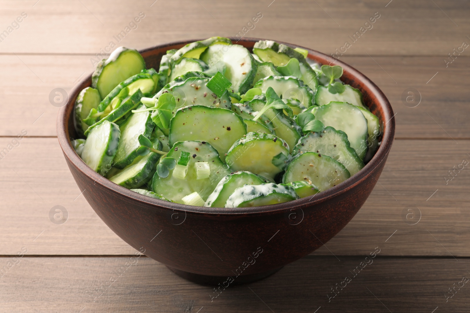 Photo of Bowl of delicious cucumber salad on wooden table, closeup