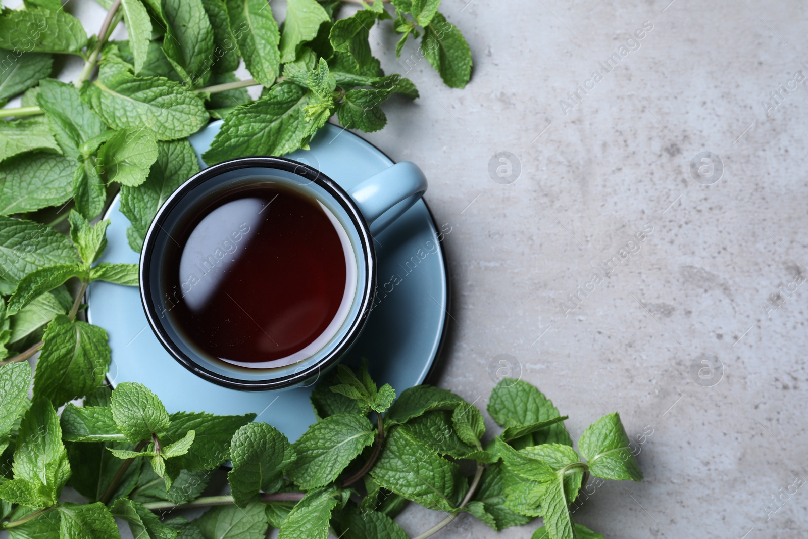 Photo of Cup with hot aromatic mint tea and fresh leaves on grey table, flat lay. Space for text