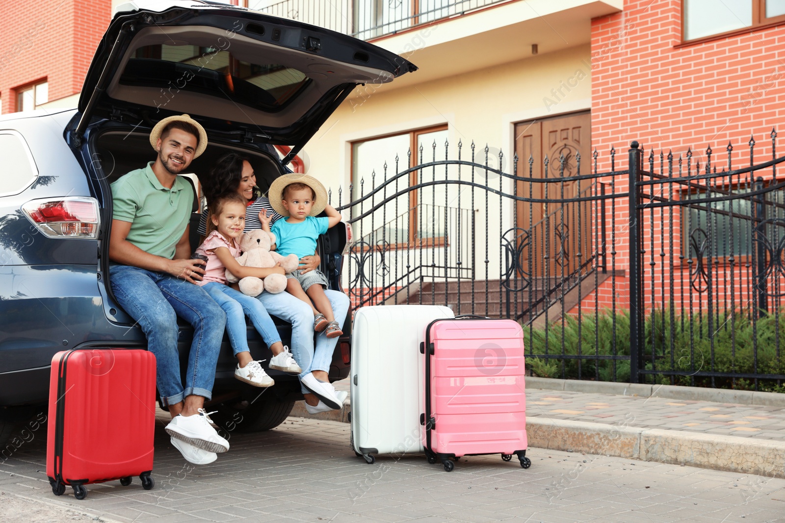 Photo of Happy family with suitcases near car in city street