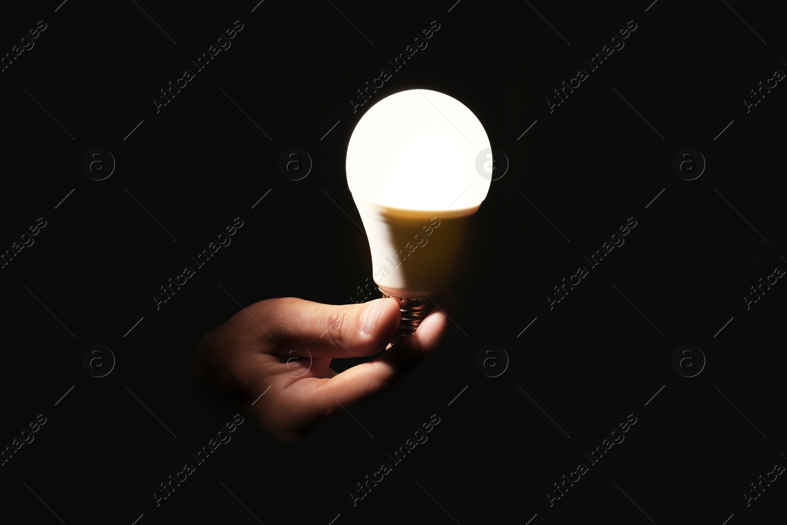 Photo of Man holding modern lamp bulb on dark background, closeup