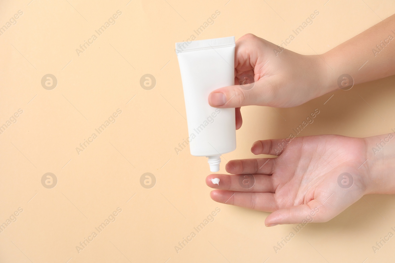 Photo of Woman applying cosmetic cream from tube onto her hand on beige background, top view. Space for text