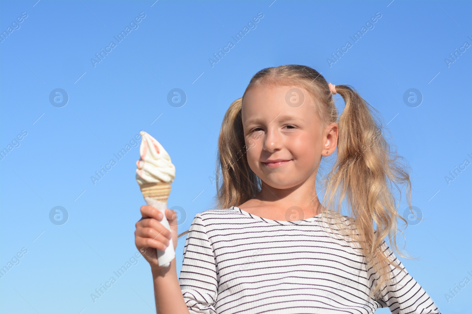 Photo of Adorable little girl with delicious ice cream against blue sky