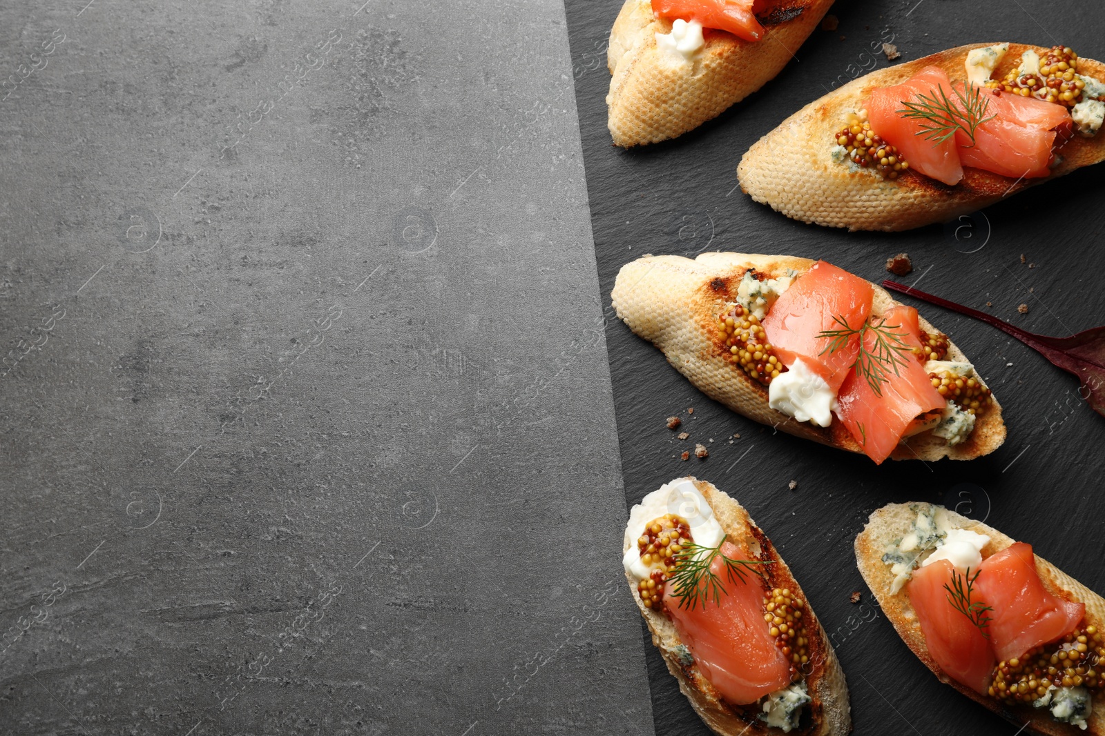 Photo of Slate plate with tasty bruschettas on grey table. Space for text