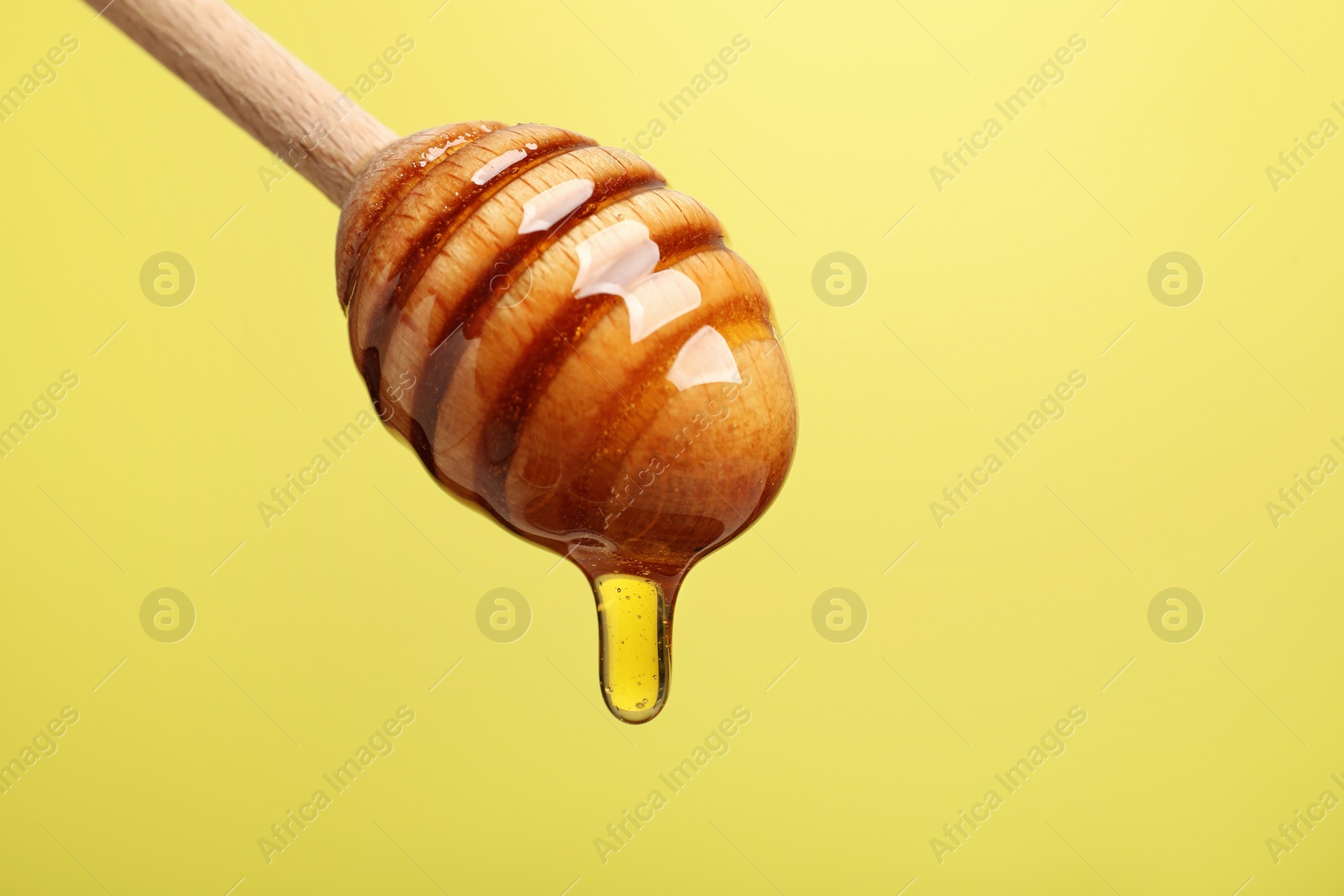 Photo of Delicious honey flowing down from dipper against yellow background, closeup. Space for text