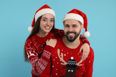 Photo of Happy young couple in Christmas sweaters and Santa hats on light blue background