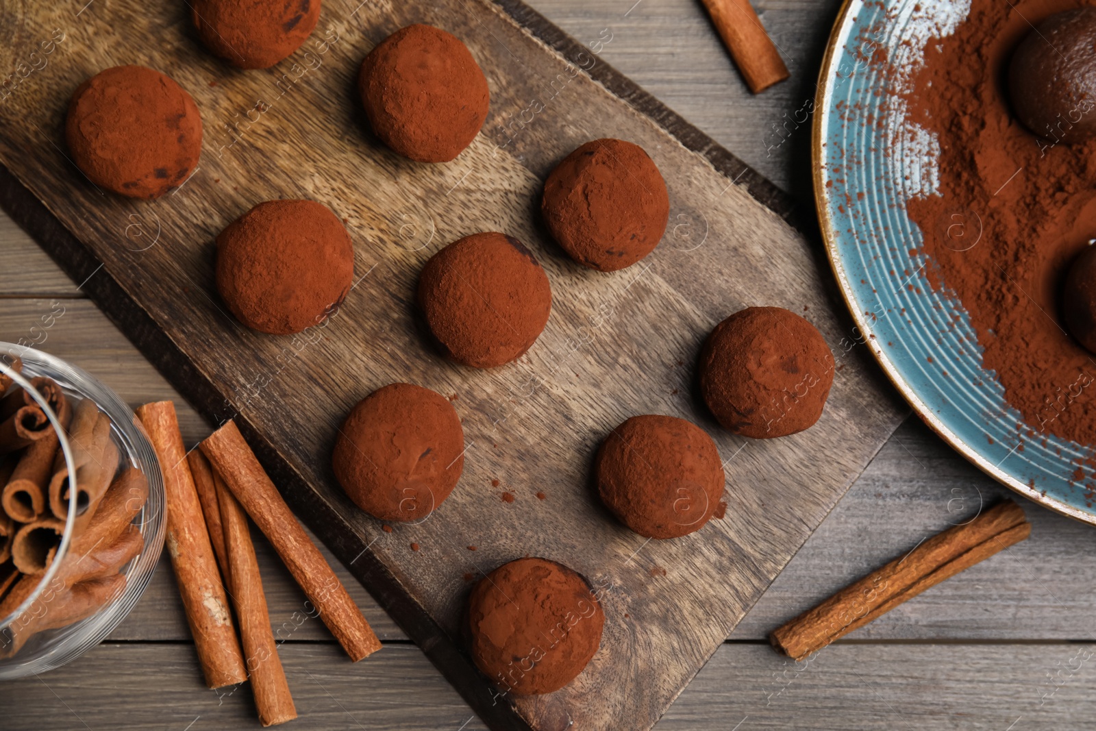 Photo of Delicious chocolate truffles with cocoa powder and cinnamon on wooden table, flat lay