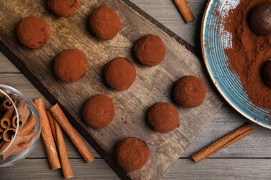 Photo of Delicious chocolate truffles with cocoa powder and cinnamon on wooden table, flat lay