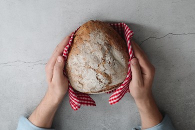 Man holding loaf of fresh bread at grey table, top view