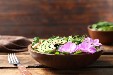 Photo of Fresh spring salad with flowers served on wooden table, closeup