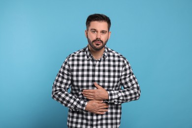 Man suffering from stomach pain on light blue background