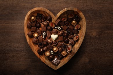 Photo of Heart shaped plate with delicious chocolate candies on wooden table, top view