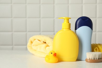 Baby cosmetic products, bath duck, brush and towel on white table against tiled wall. Space for text