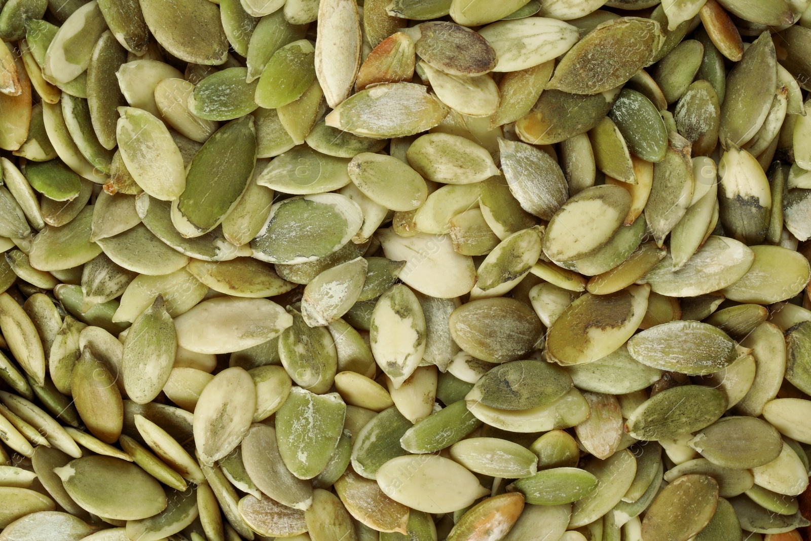 Photo of Many peeled pumpkin seeds as background, top view