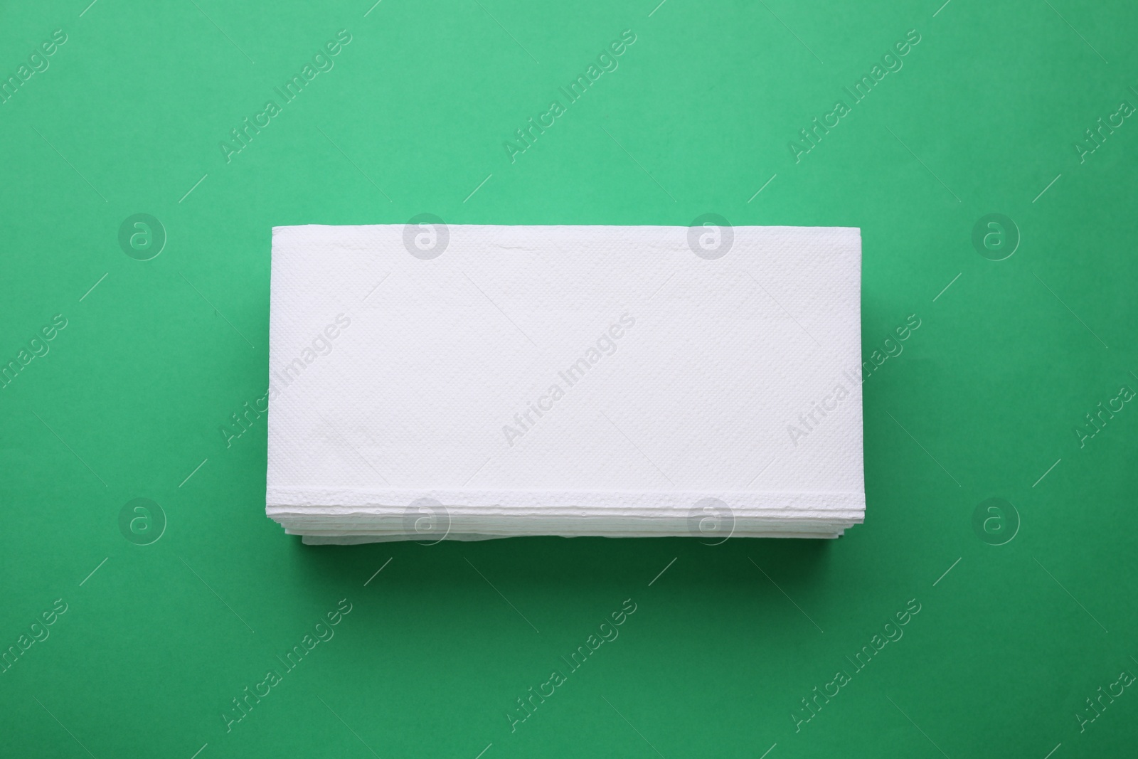 Photo of Stack of clean tissue towels on green background, top view