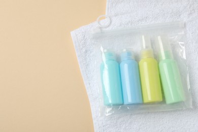 Cosmetic travel kit and towel on beige background, top view with space for text. Bath accessories