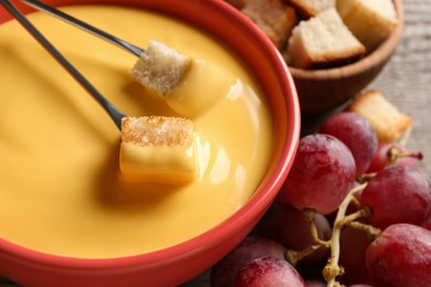 Pot of tasty cheese fondue, forks with bread pieces and grapes on table, closeup