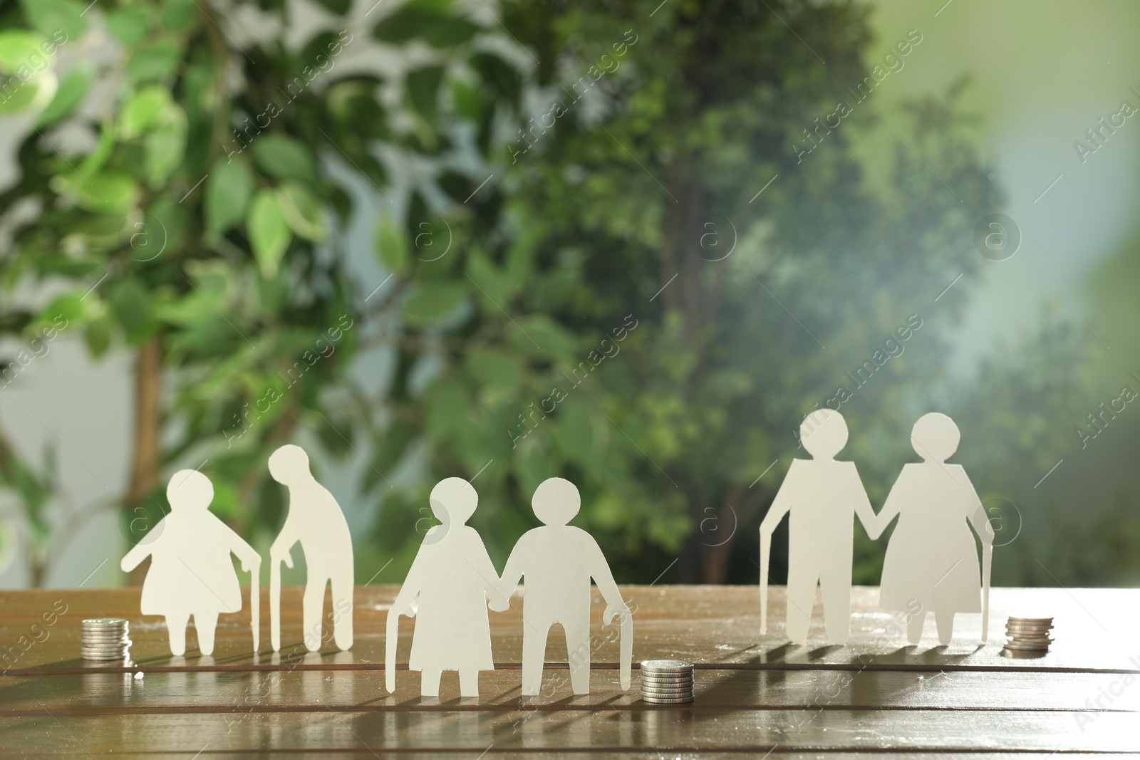 Photo of Pension savings. Figures of elderly people and coins on wooden table outdoors