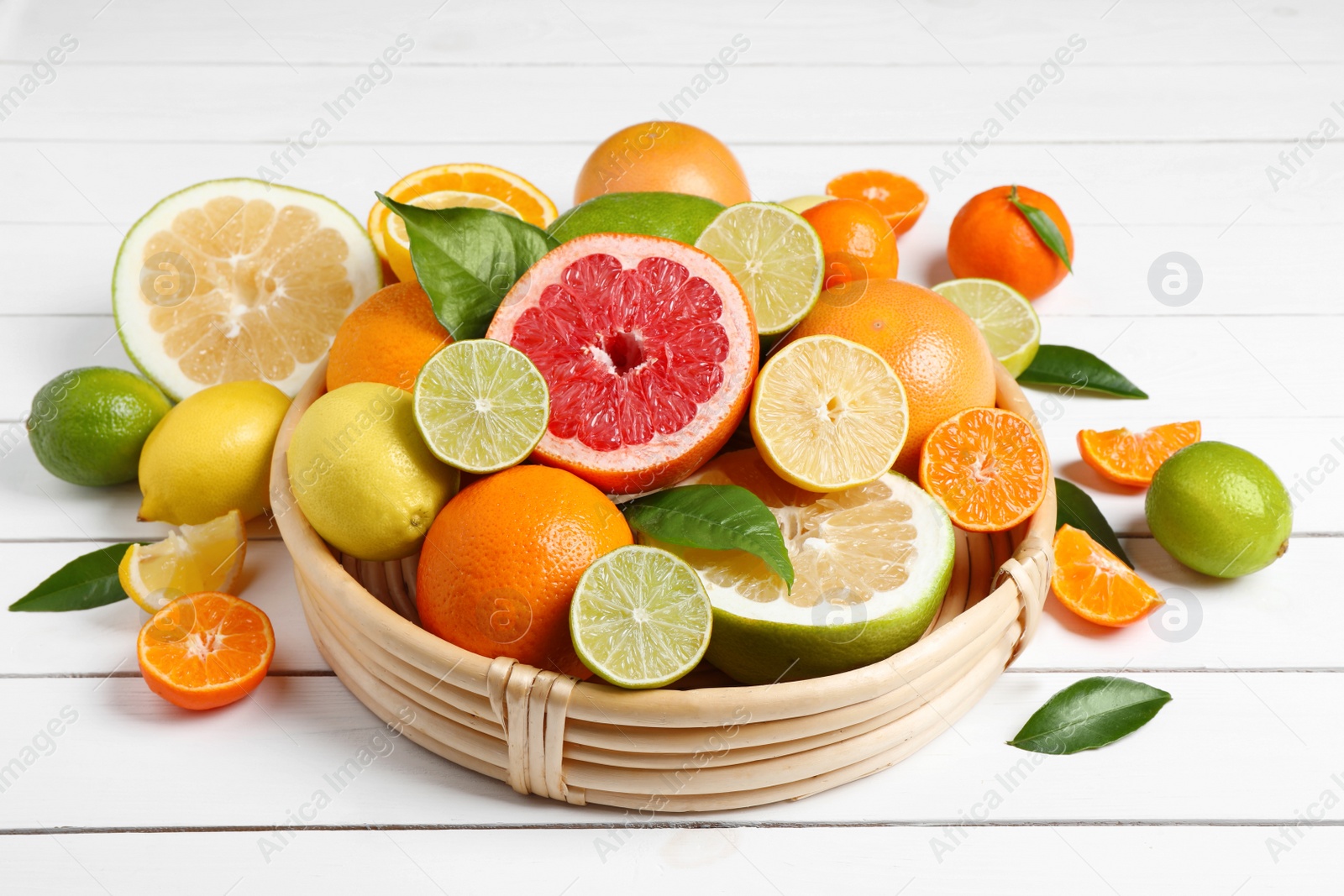 Photo of Different ripe citrus fruits with green leaves on white wooden table