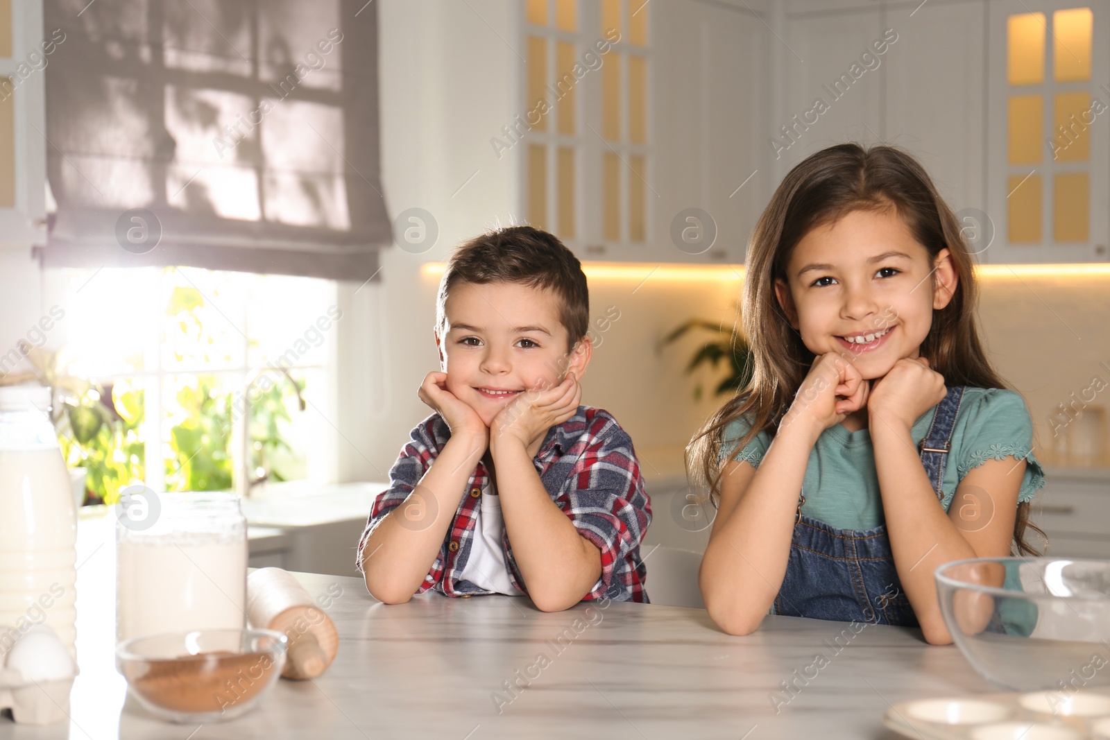 Photo of Cute little children at table with cooking ingredients in kitchen