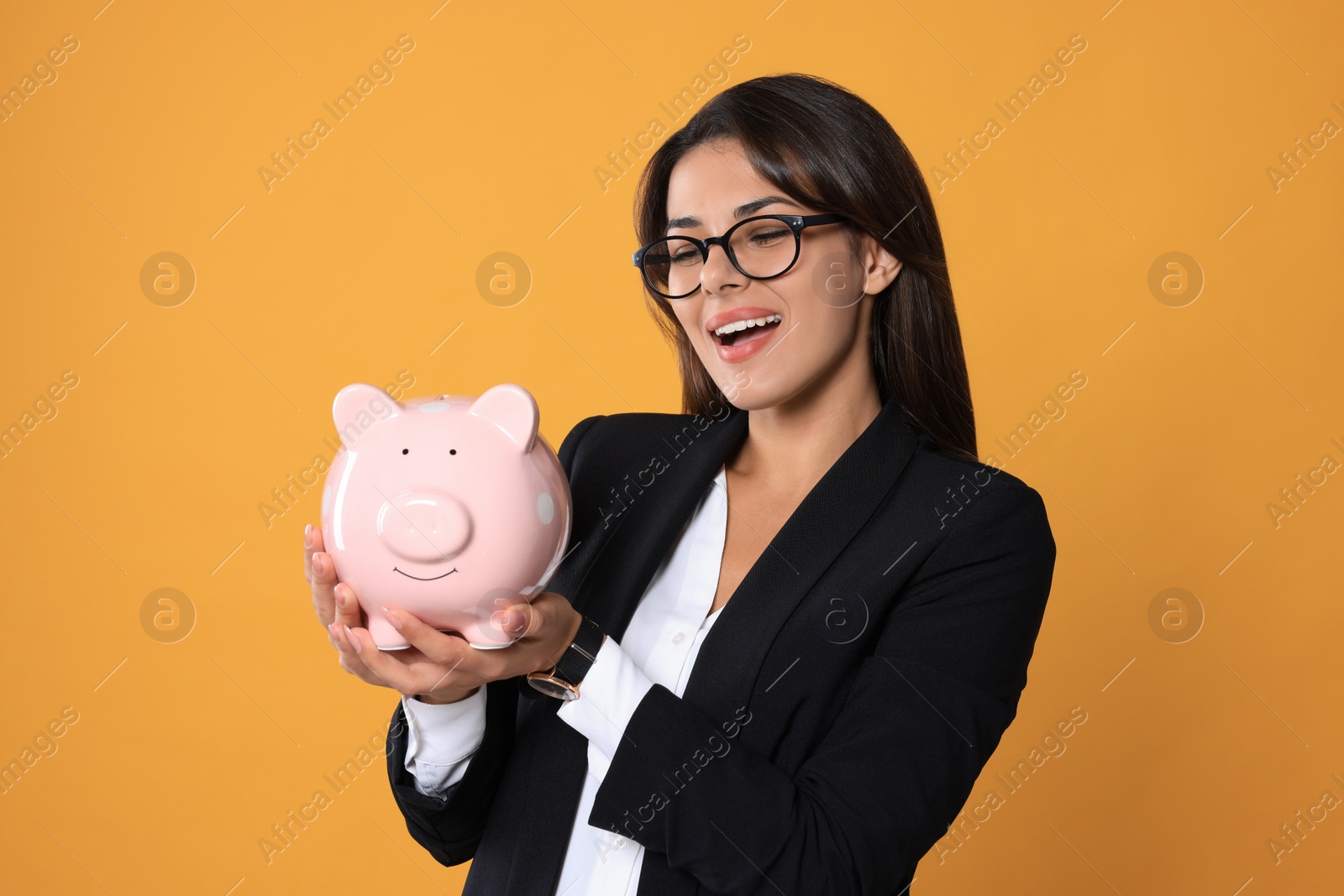 Photo of Young woman in eyeglasses with piggy bank on orange background