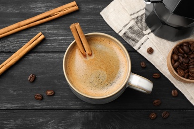 Photo of Cup of hot coffee with aromatic cinnamon on black wooden table, flat lay