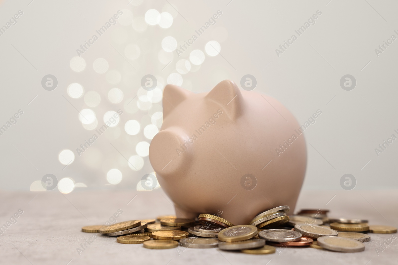 Photo of Piggy bank and coins on grey table against blurred lights