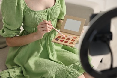Photo of Beauty blogger reviewing eyeshadows and recording video with smartphone and ring lamp at home, closeup