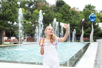 Photo of Attractive woman taking selfie near fountain in park