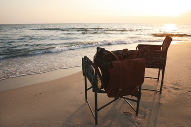 Photo of Camping chairs and backpack on sandy beach near sea, space for text