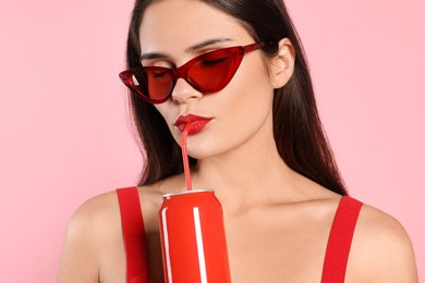 Photo of Beautiful young woman with stylish sunglasses drinking from tin can on pink background