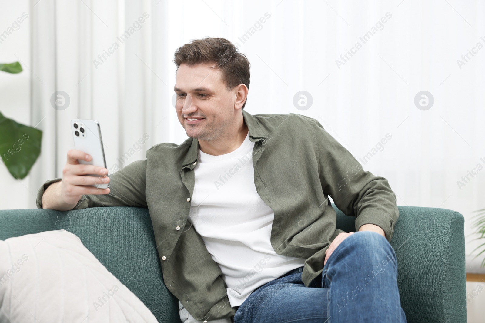 Photo of Happy man using smartphone on sofa at home