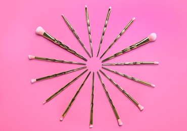 Photo of Set of makeup brushes on pink background, flat lay