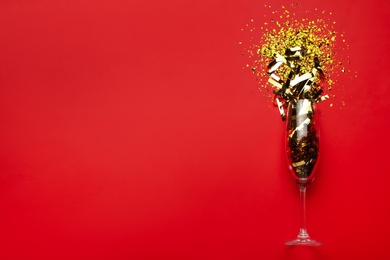 Photo of Flat lay composition with confetti and champagne glass on red background. Space for text