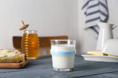 Glass with milk, honey, bread and butter on grey wooden table