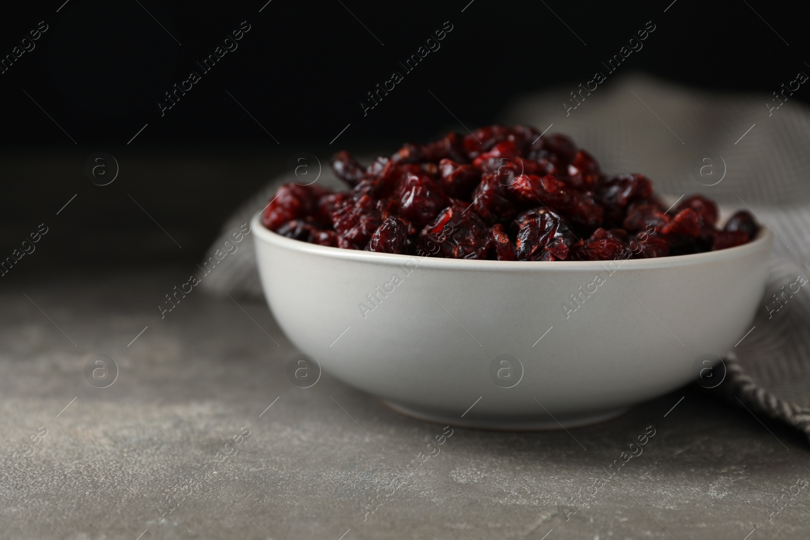 Photo of Bowl of dried cranberries on grey table, closeup
