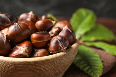 Photo of Delicious roasted edible chestnuts in wooden bowl, closeup