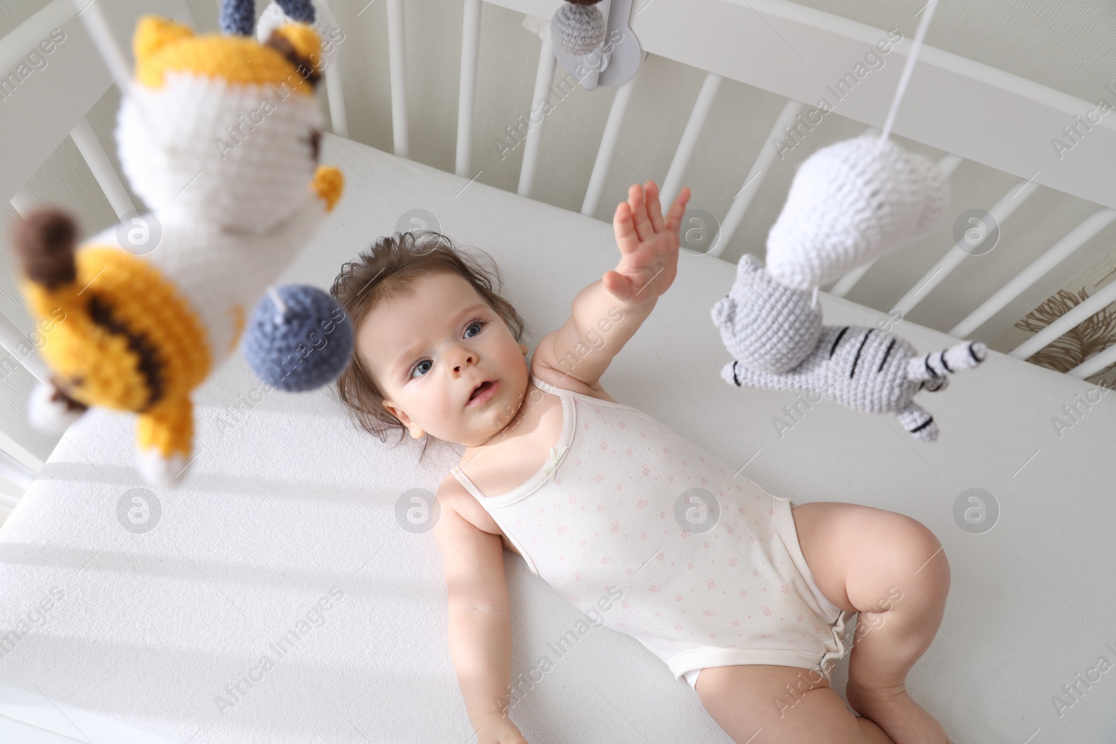 Photo of Cute little baby looking at hanging mobile in crib, top view