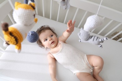 Cute little baby looking at hanging mobile in crib, top view