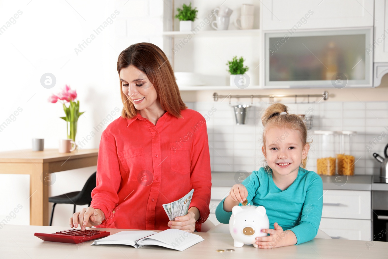 Photo of Mother and daughter with money at table in kitchen. Saving money