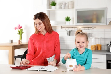 Photo of Mother and daughter with money at table in kitchen. Saving money