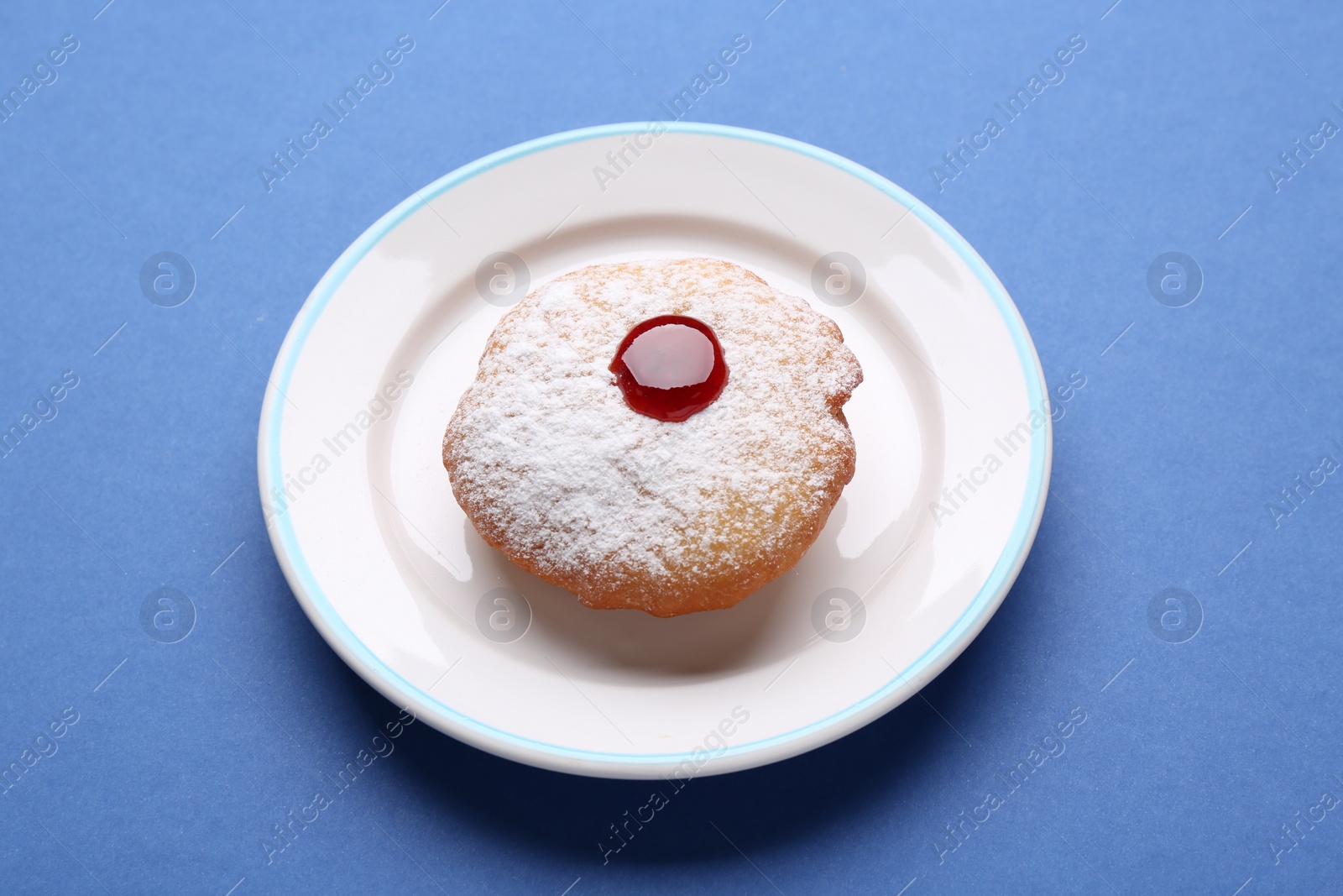 Photo of Hanukkah donut with jelly and powdered sugar on blue background