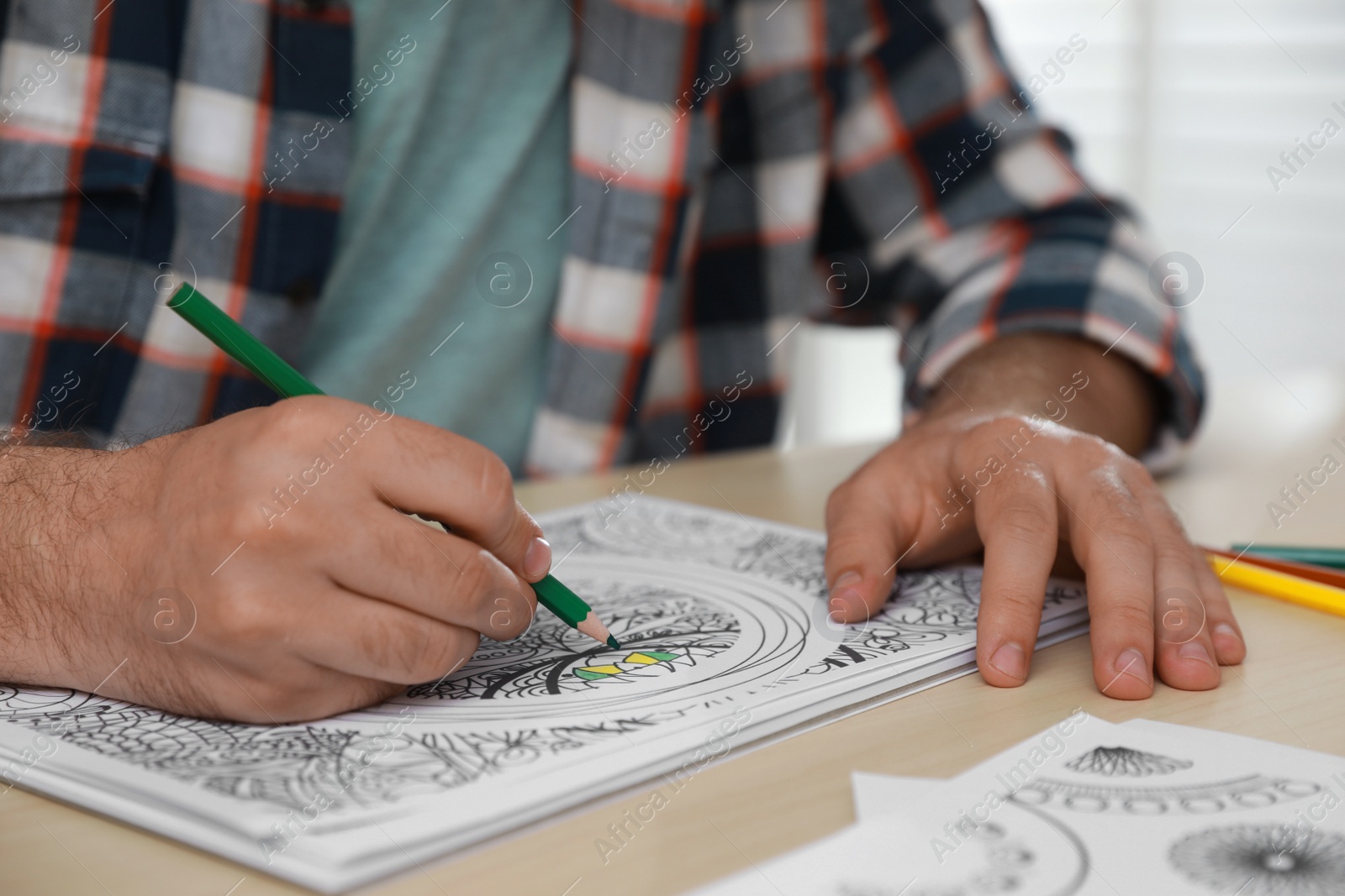 Photo of Man coloring antistress picture at table indoors, closeup