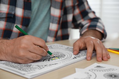 Man coloring antistress picture at table indoors, closeup