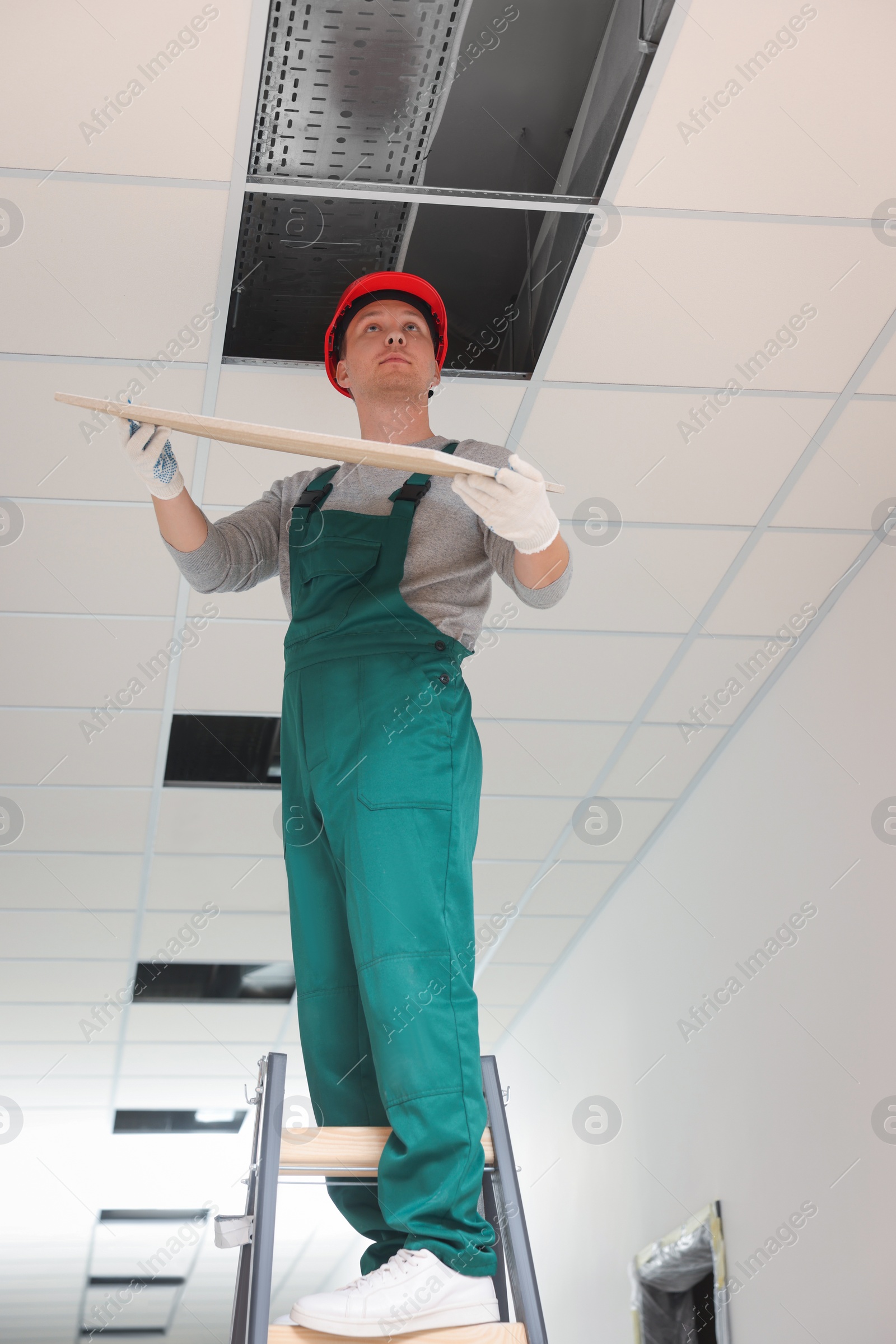 Photo of Suspended ceiling installation, low angle view. Builder working with PVC tile