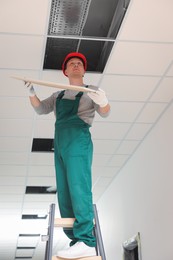 Photo of Suspended ceiling installation, low angle view. Builder working with PVC tile