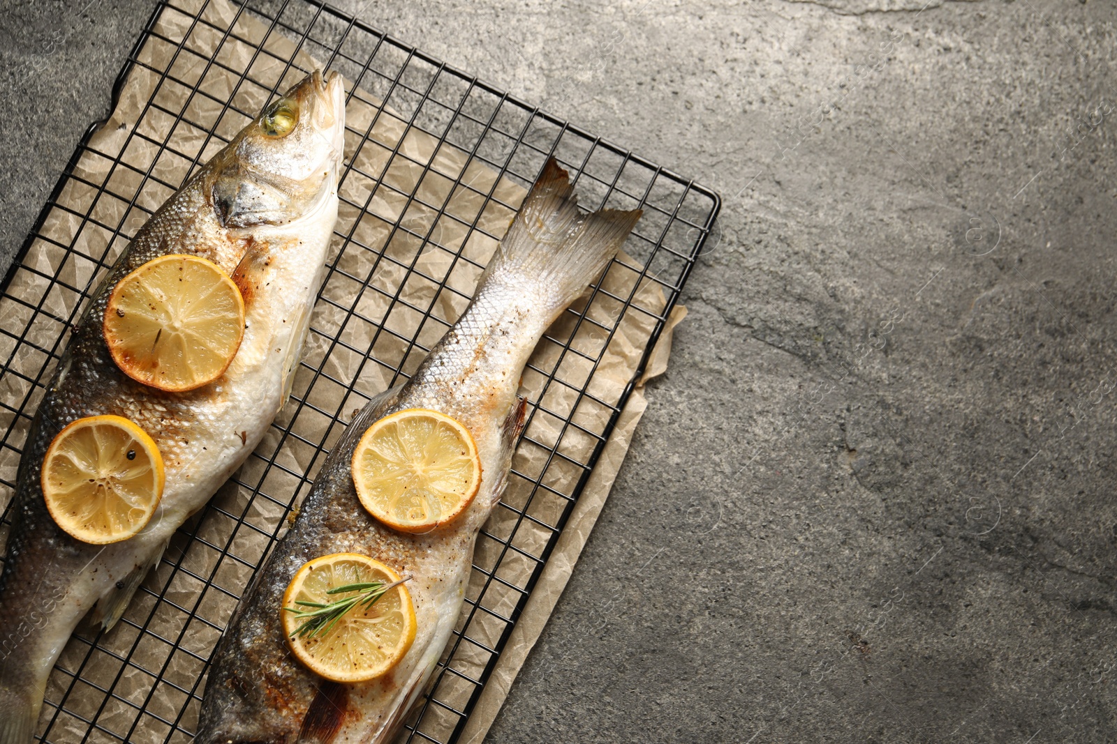 Photo of Baked fish with lemon on grey textured table, top view. Space for text