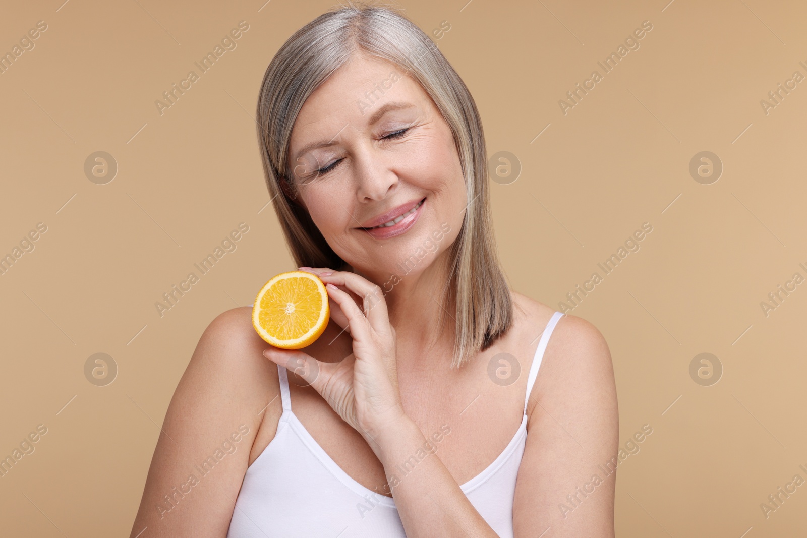 Photo of Beautiful woman with half of orange rich in vitamin C on beige background